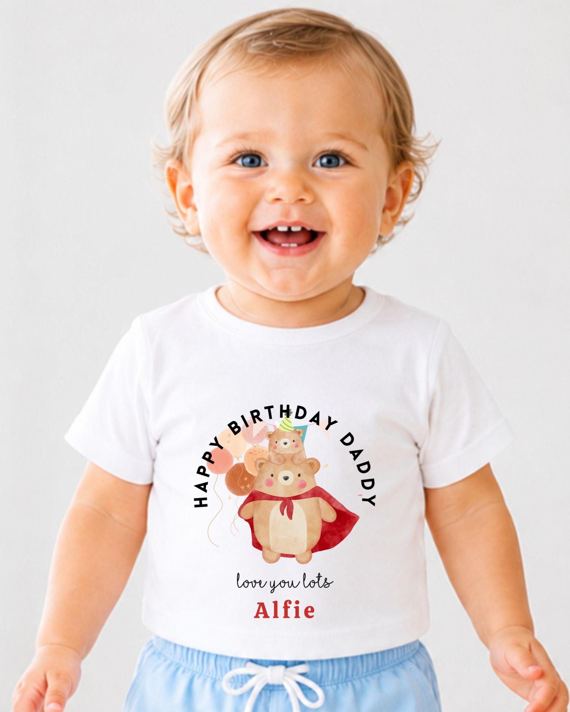 A smiling baby boy wearing a white t-shirt with a birthday message and a cartoon bear graphic.