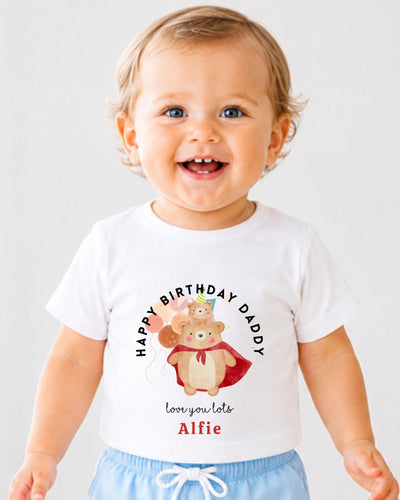 A smiling baby boy wearing a white t-shirt with a birthday message and a cartoon bear graphic.