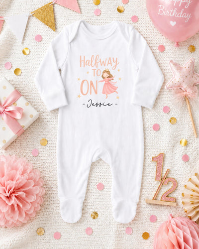 A white onesie with a cartoon character printed on it, surrounded by pink and gold confetti, a pink balloon, and other birthday decorations.