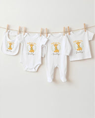 A row of four white baby clothes with a giraffe design, hanging on a clothesline.