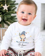 A smiling baby boy wearing a white sweater with a gnome graphic and text that says "My first Christmas Hudson 20x".