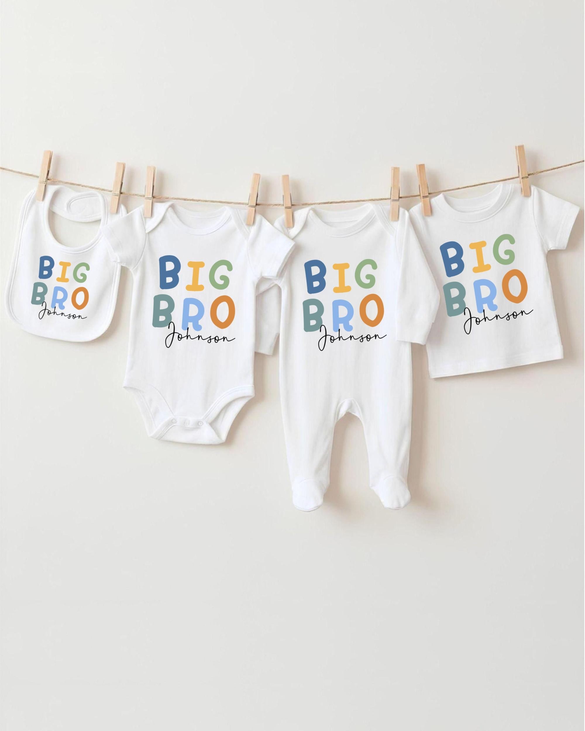 A row of four white baby clothes with the text "BIG BRO Johnson" printed on them, hanging on a clothesline.