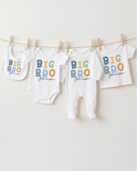 A row of four white baby clothes with the text "BIG BRO Johnson" printed on them, hanging on a clothesline.