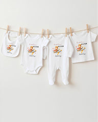 A row of four white baby clothes, including onesies and bibs, hanging on a clothesline.