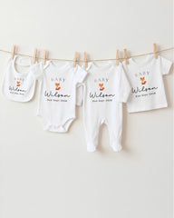 A row of four white baby clothes with the name "Baby Wilson" printed on them, hanging on a clothesline.