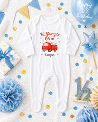 A white onesie with a red firetruck design, surrounded by birthday decorations, confetti, and a balloon, all arranged on a white background.
