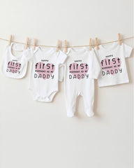 A row of white baby clothes with the text "Happy first birthday as my Daddy" printed on them, hanging on a clothesline.