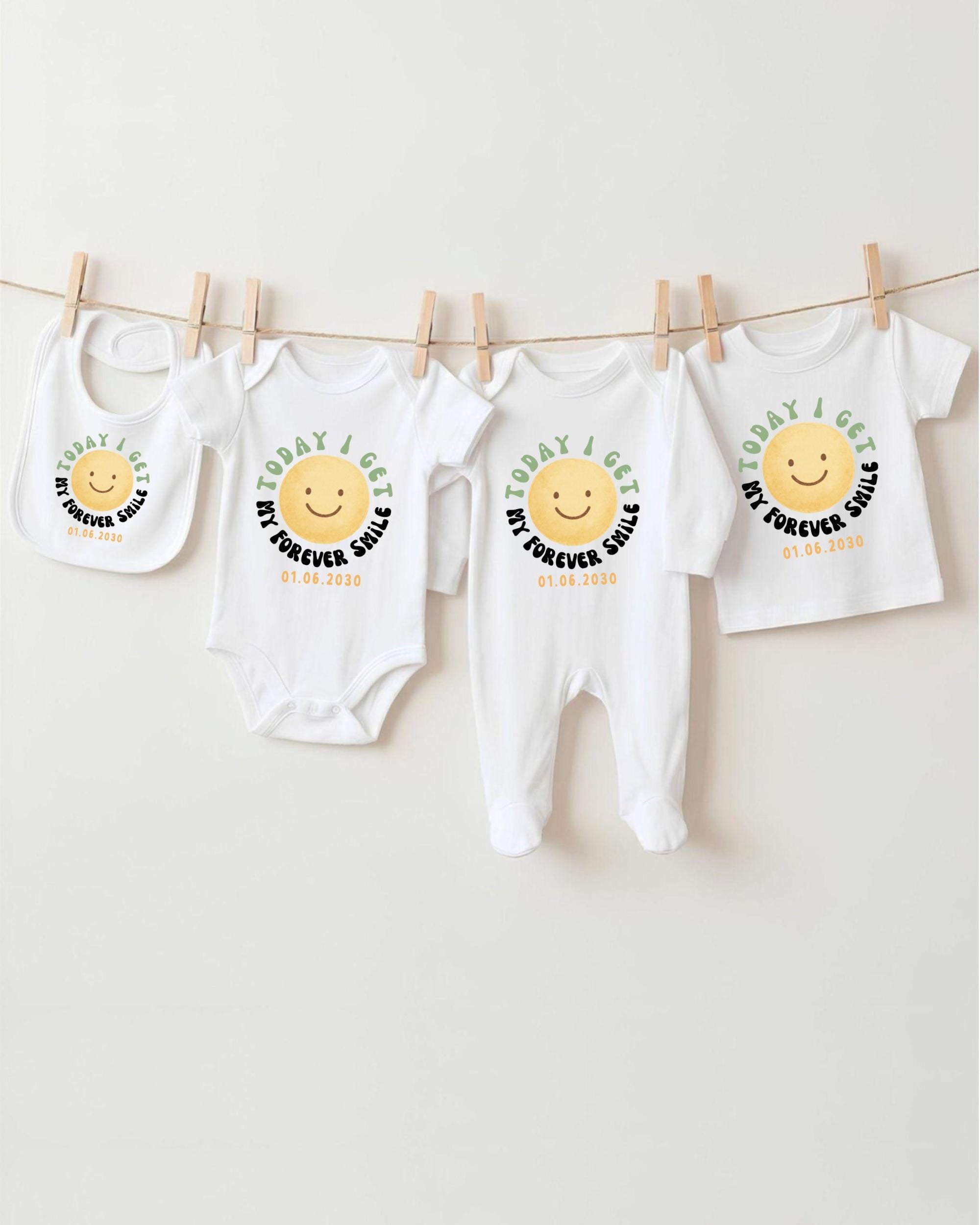 A row of four white baby clothes with a cheerful smiley face design, hanging on a clothesline.