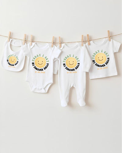 A row of four white baby clothes with a cheerful smiley face design, hanging on a clothesline.