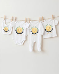 A row of four white baby clothes with a cheerful smiley face design, hanging on a clothesline.