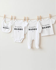 A row of four white baby clothes with the text "You're going to be a DADDY" printed on them, hanging on a clothesline.