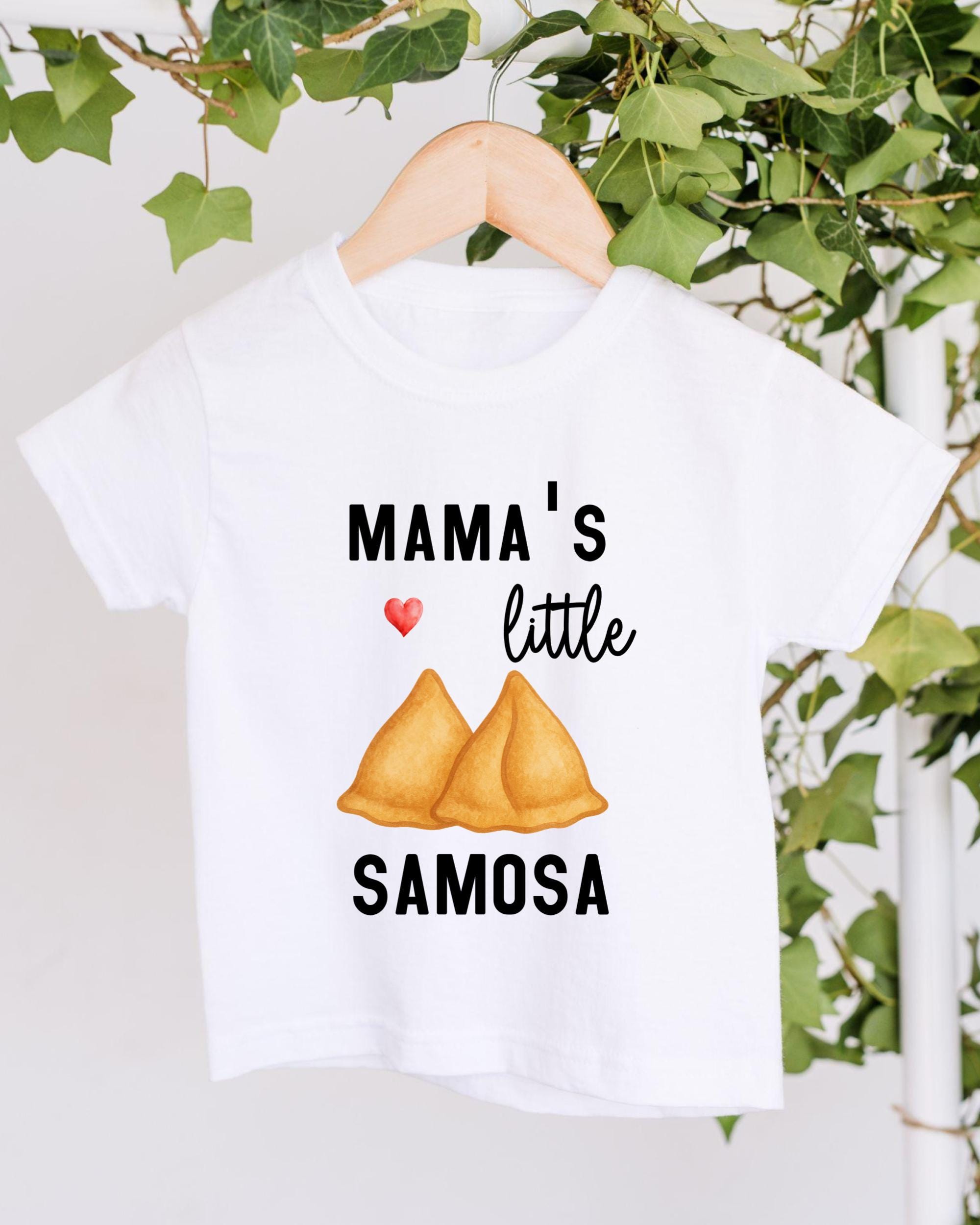 A white t-shirt with a graphic design featuring a heart symbol and the text "MAMA'S little SAMOSA" printed on it.