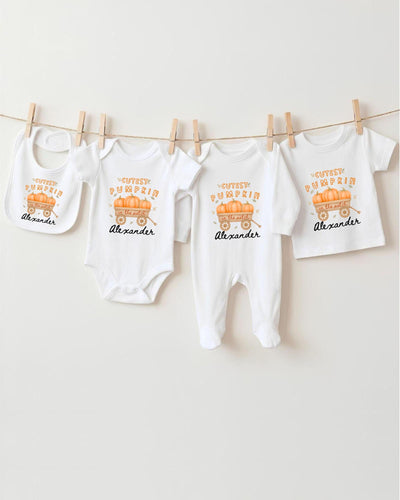 A row of white baby clothes with a pumpkin theme, including bibs and bodysuits, hanging on a clothesline.