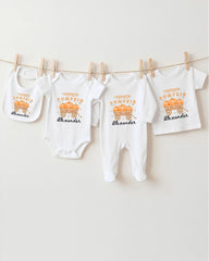 A row of white baby clothes with a pumpkin theme, including bibs and onesies, hanging on a clothesline.