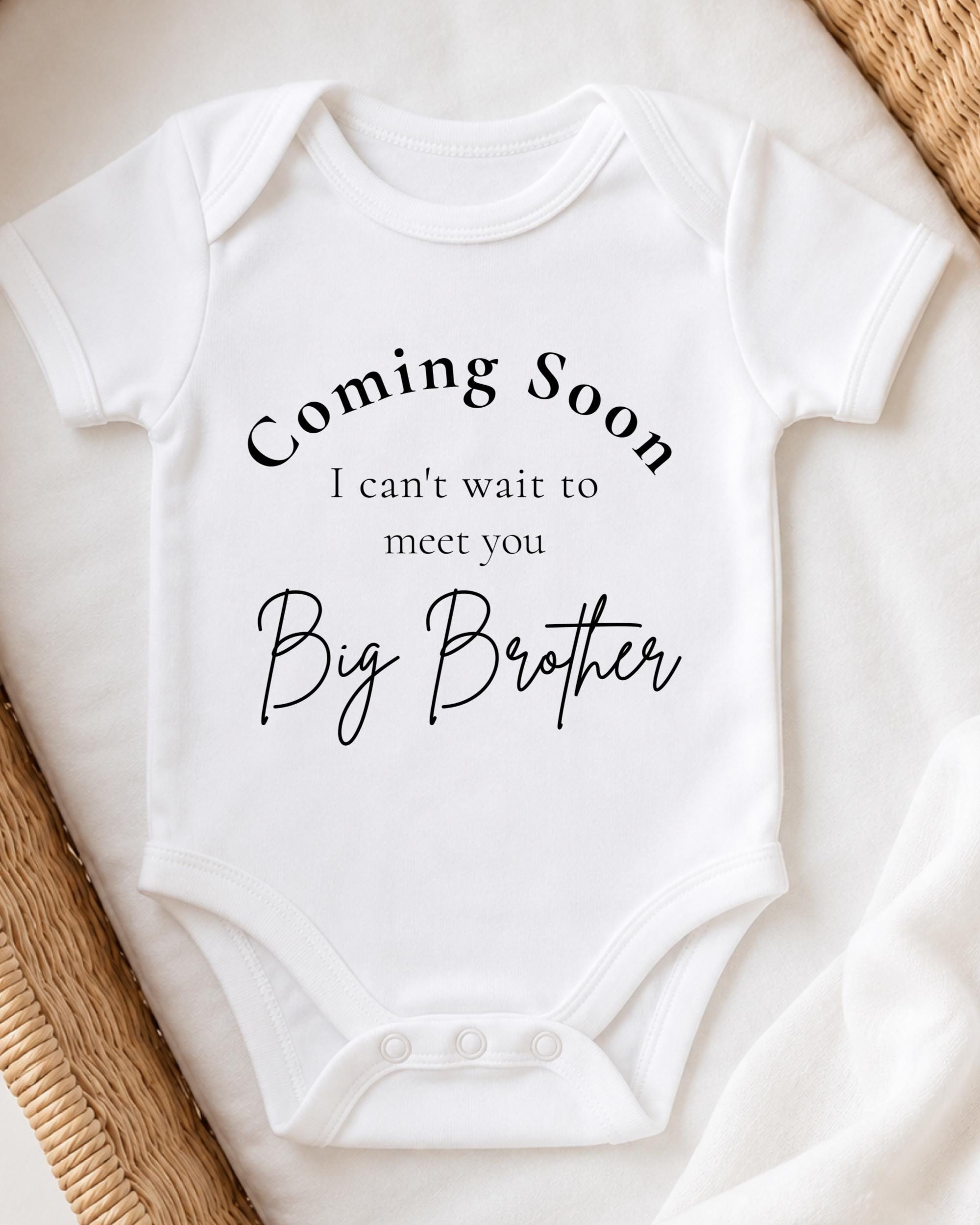 A white baby onesie with text that says "Coming Soon I can't wait to meet you Big Brother".