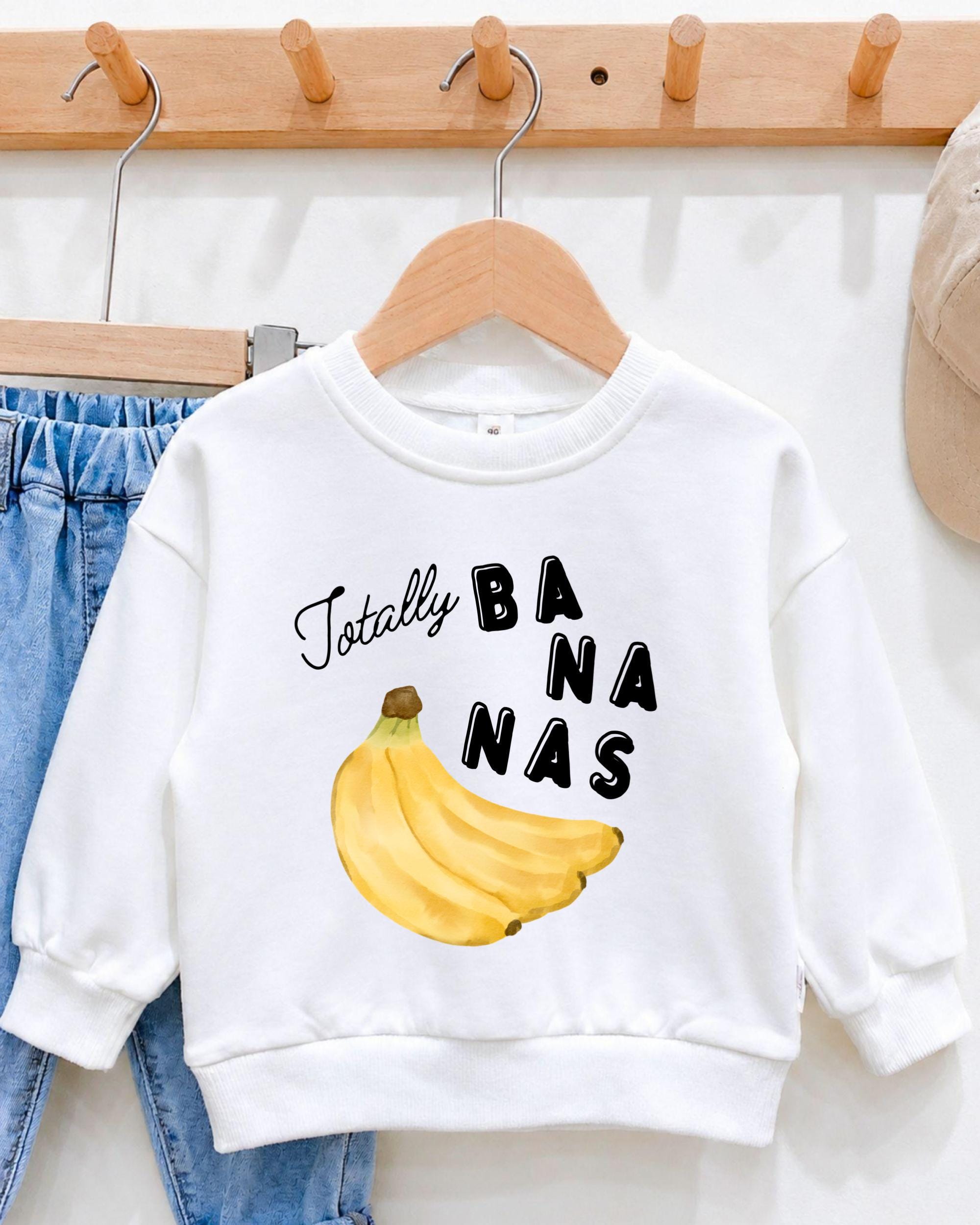 A white sweatshirt with a graphic of a banana and the text "Totally BANANA" printed on it, hanging on a wooden hanger.