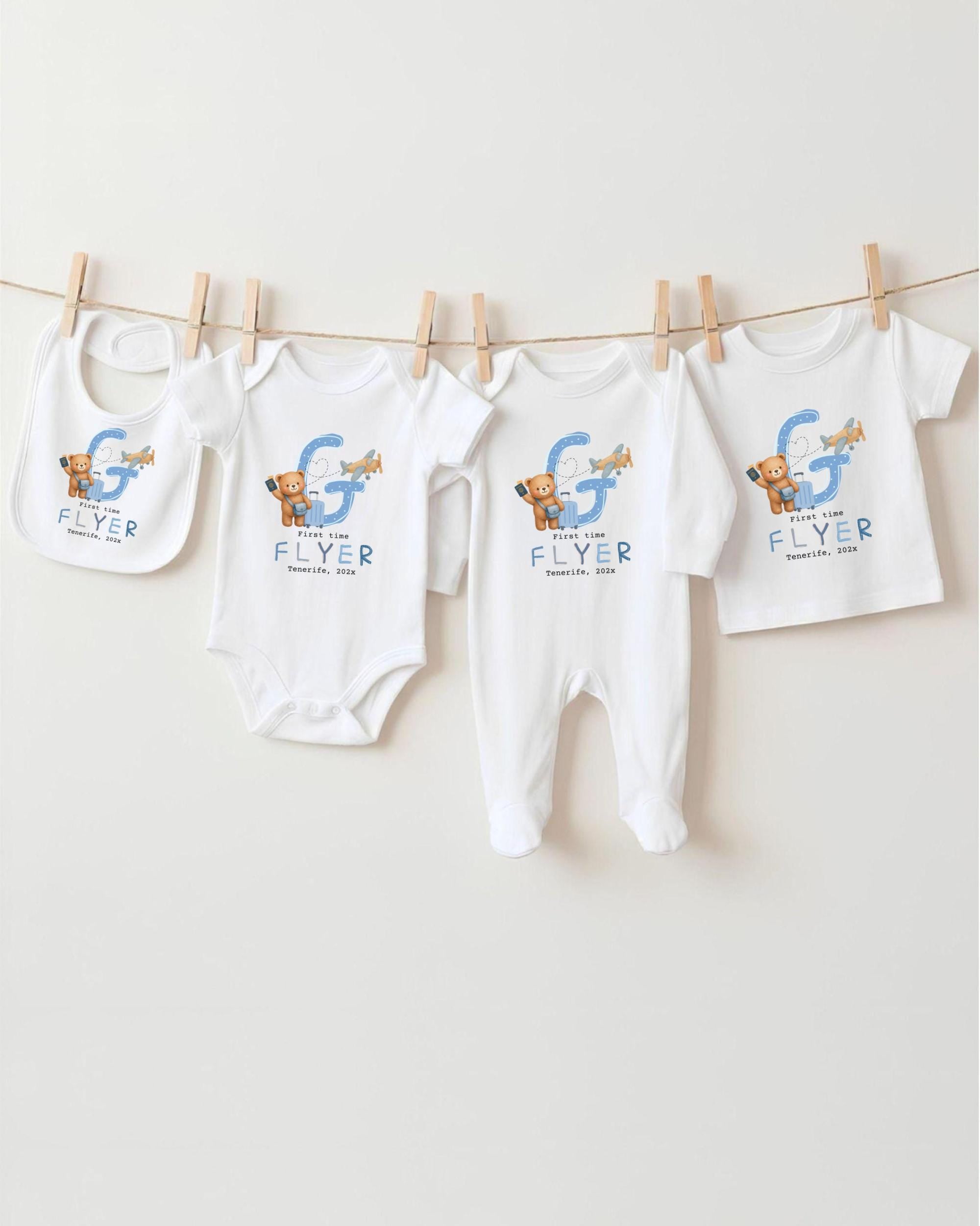 A collection of baby clothes, including onesies and bibs, hanging on a clothesline.