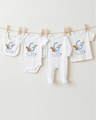 A collection of baby clothes, including onesies and bibs, hanging on a clothesline.