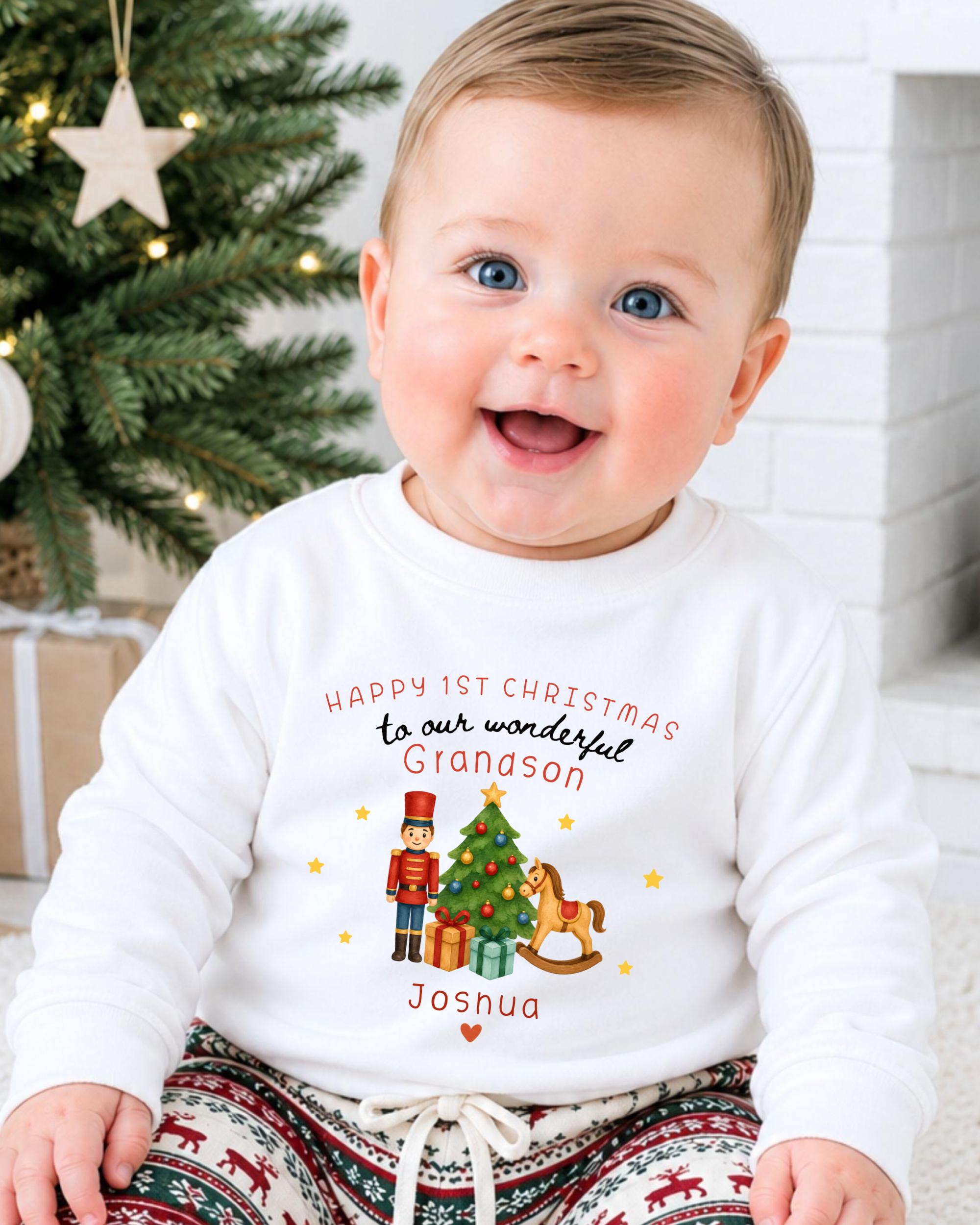 A smiling baby wearing a white sweatshirt with a Christmas-themed design and text.