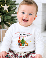A smiling baby wearing a white sweatshirt with a Christmas-themed design and text.