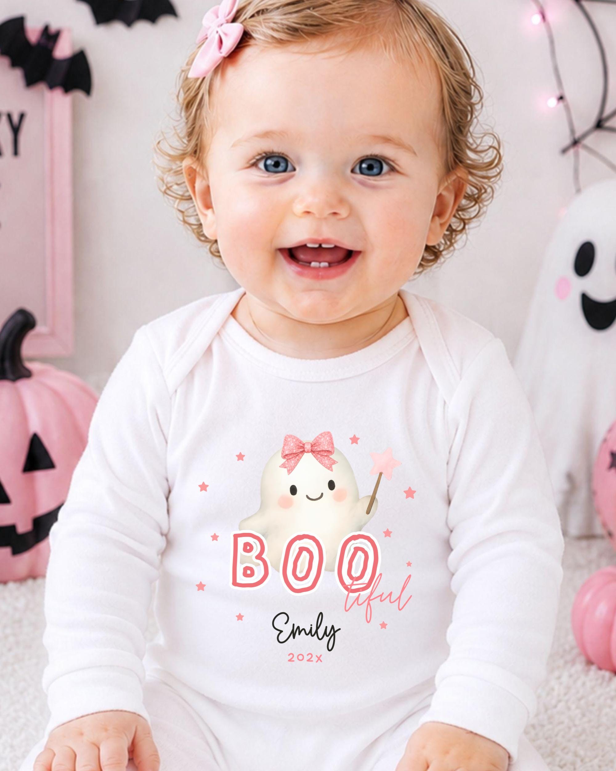 A smiling baby girl wearing a white onesie with a ghost character and the text "BOO" and "Emilly 2020" printed on it.