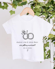 A white t-shirt with a graphic design and text printed on it, hanging on a wooden hanger.