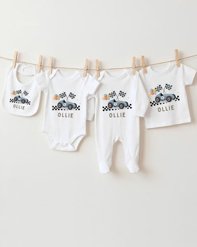 A collection of white baby clothes, including bodysuits and bibs, with a racing car design, hanging on a clothesline.