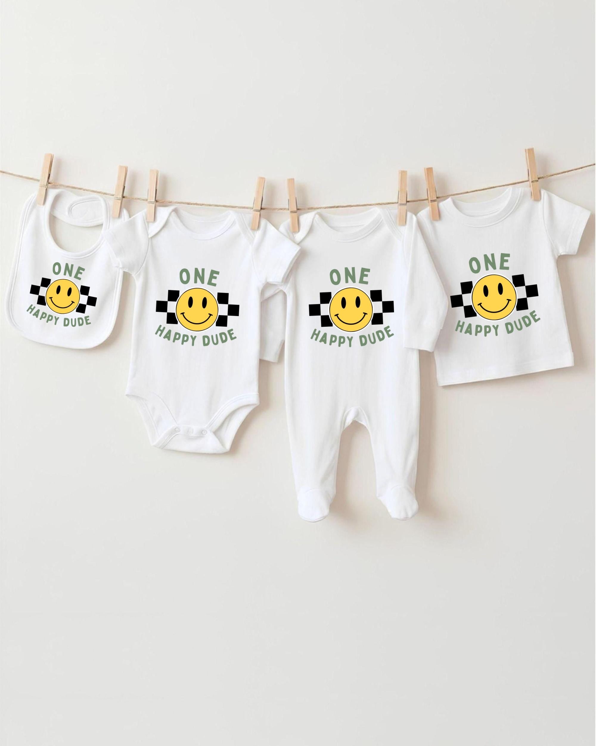 A collection of four white baby clothes with a cheerful yellow smiley face design, hanging on a clothesline.