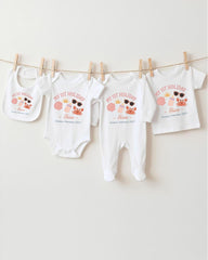 A collection of baby clothes, including onesies and bibs, hanging on a clothesline.
