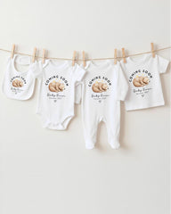 A row of white baby clothes with the text "Coming Soon Baby Girl" printed on them, along with a bear image.