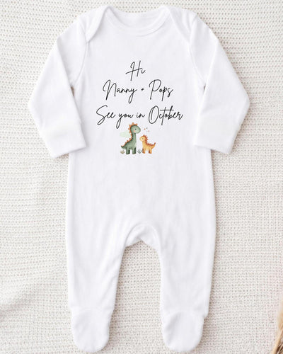 A white bodysuit with a printed message that reads "Hi Nanny + Pops See you in October" along with two cartoon dinosaur illustrations.