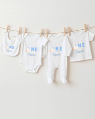 A collection of white baby clothes, including onesies and bibs, hanging on a clothesline.