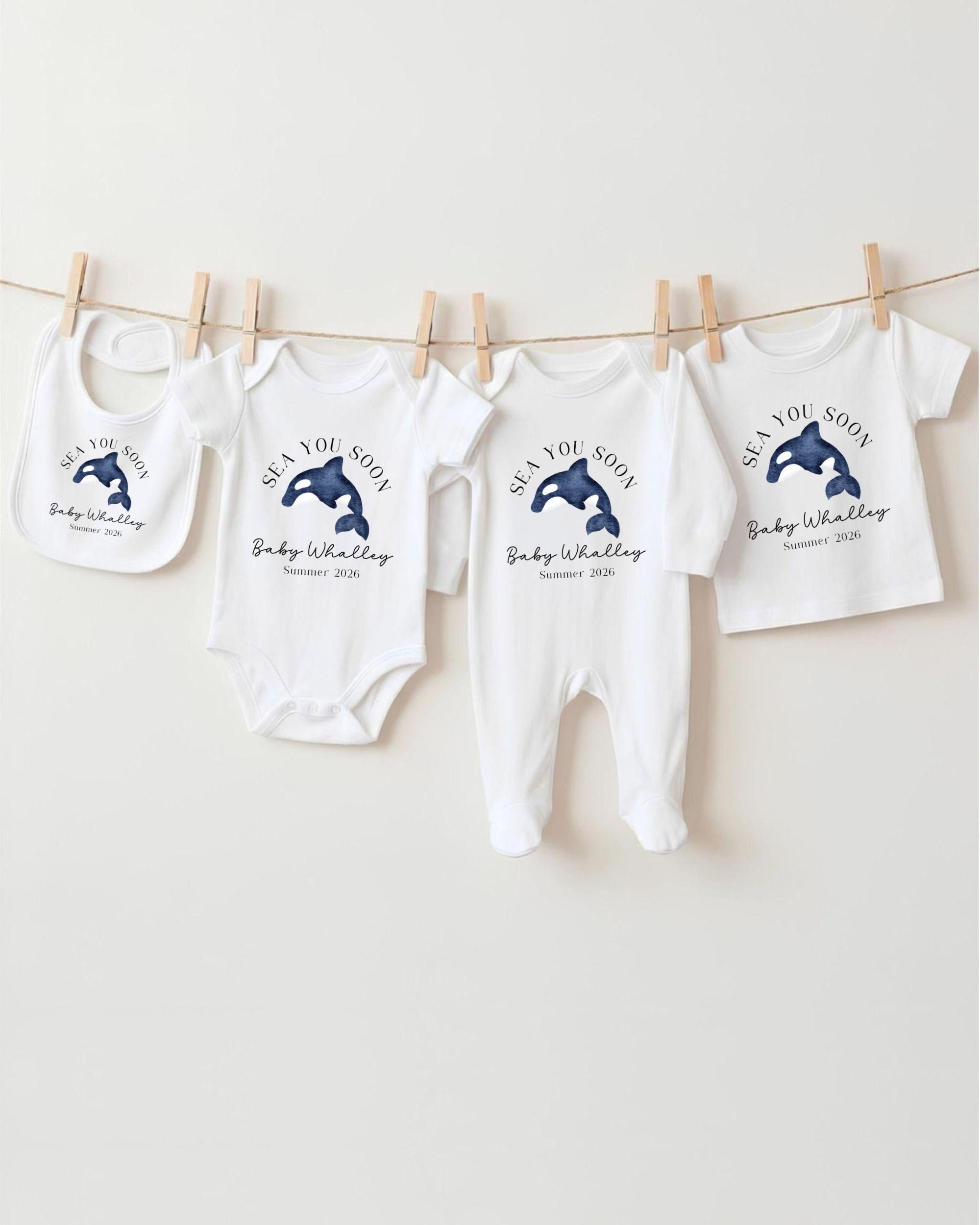 A row of white baby clothes with blue whale designs, including bibs and onesies, hanging on a clothesline.