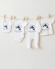 A row of white baby clothes with blue whale designs, including bibs and onesies, hanging on a clothesline.