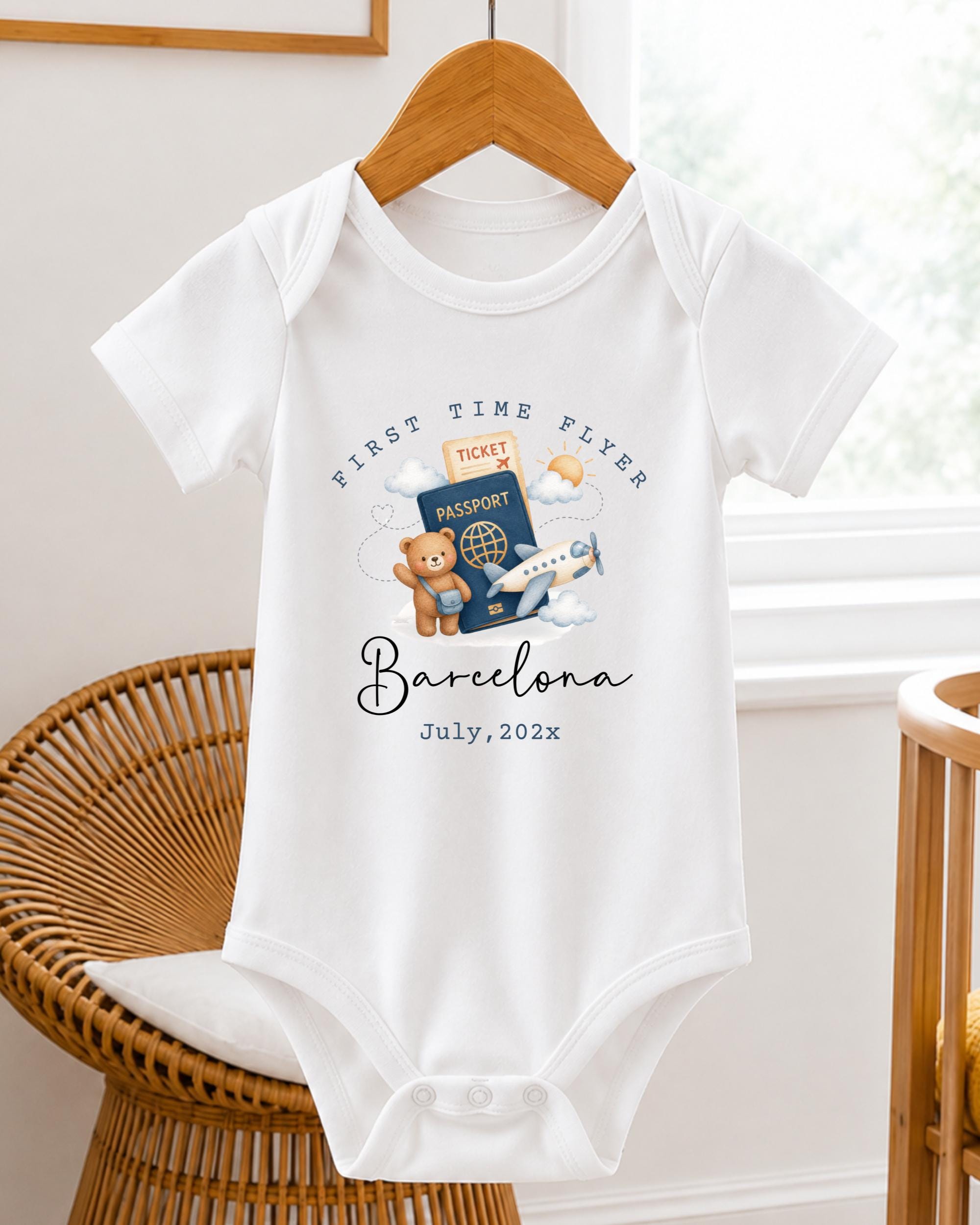 A white baby onesie with a graphic design of a teddy bear, a passport, and an airplane, along with the text "First Time Flyer Barcelona July, 2023".