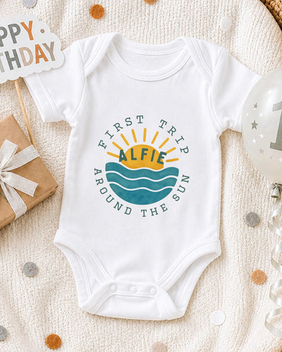 A white bodysuit with a graphic design on it, surrounded by a gift box, a birthday balloon, and confetti.