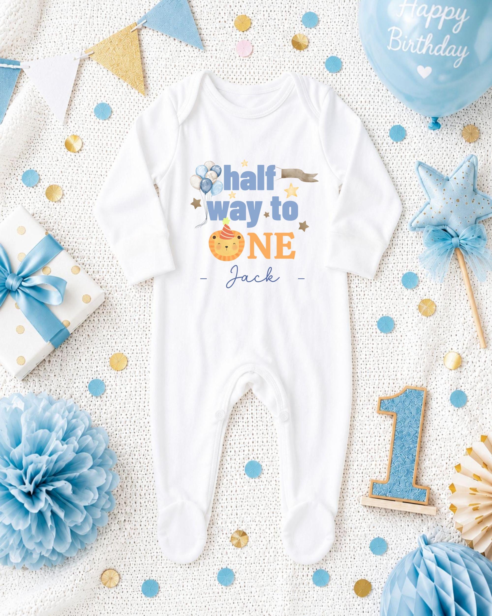 A white onesie with the text "half way to one" printed on it, surrounded by birthday decorations such as a blue balloon, blue and gold confetti, and a blue and gold star.