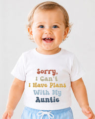 A smiling baby wearing a white t-shirt with text that says "Sorry, I Can't Have Plans With My Auntie".