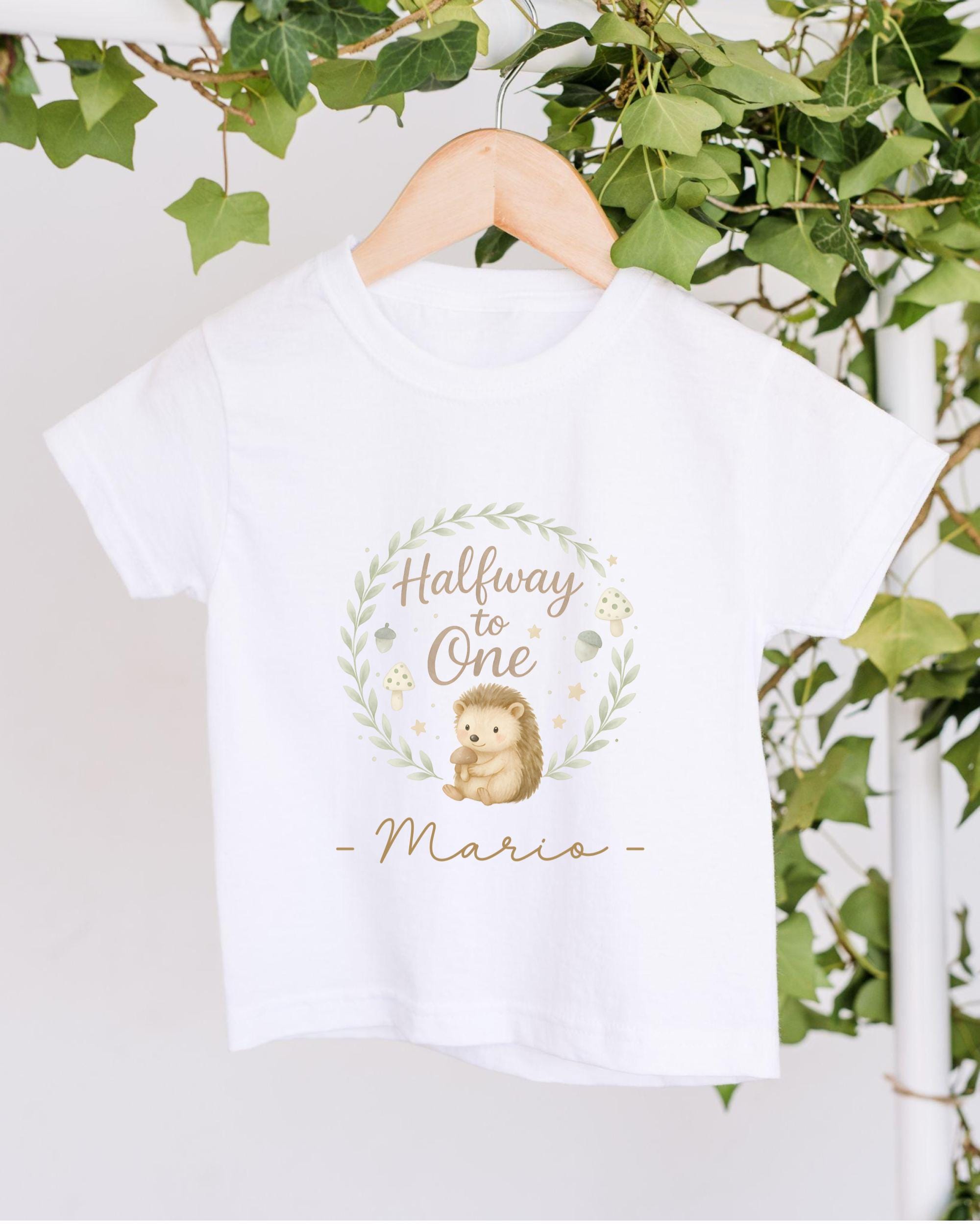 A white t-shirt with a graphic design featuring a hedgehog and the text "Halfway to One - Mario" hanging on a wooden hanger.