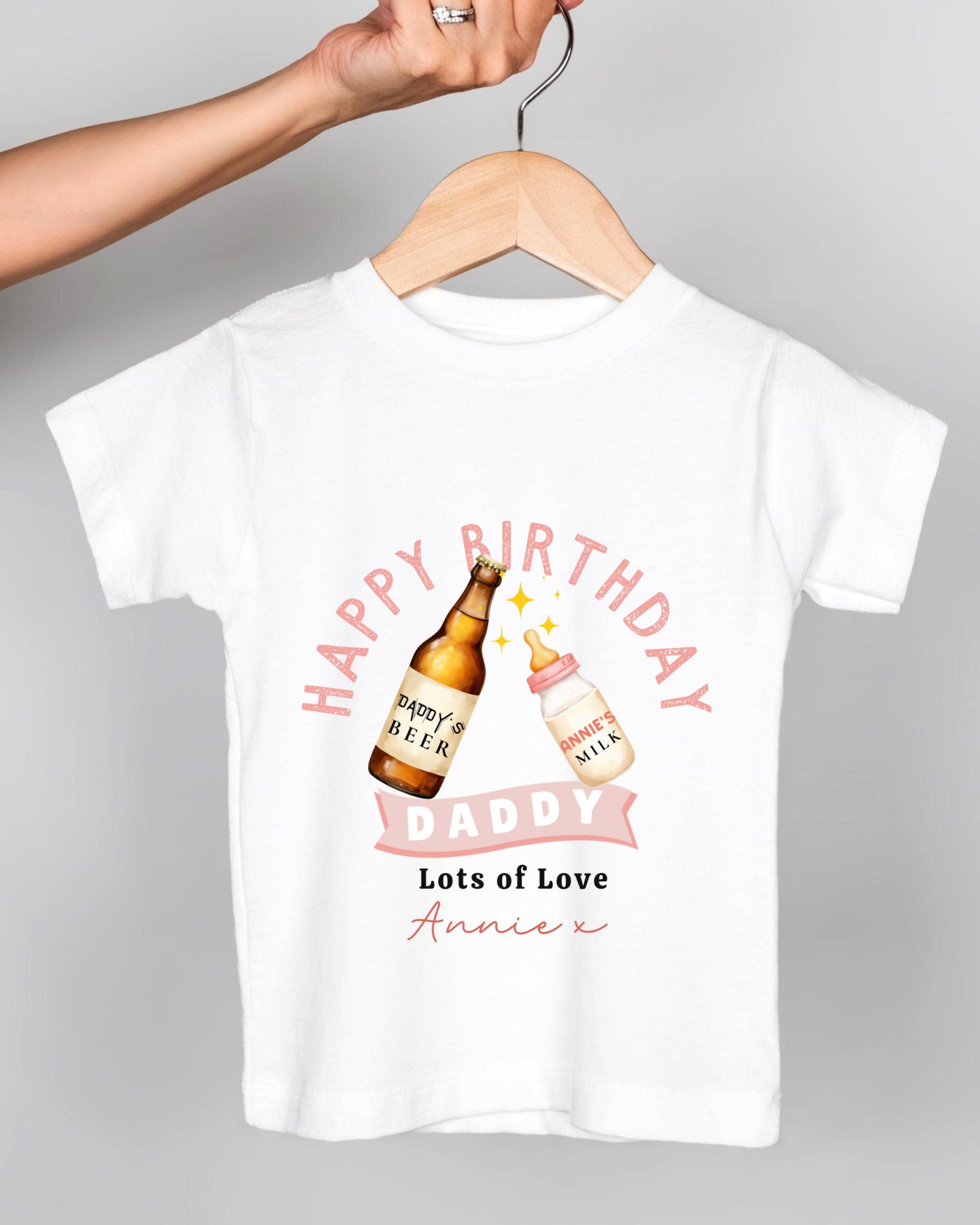 A white t-shirt with a graphic design featuring a bottle of beer and a baby bottle, along with the text "Happy Birthday Daddy Lots of Love Annie" printed on it.