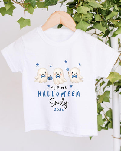 A white t-shirt with a Halloween-themed design featuring three cute ghost characters and stars. The text on the t-shirt reads "My First Halloween Emily 2020x".