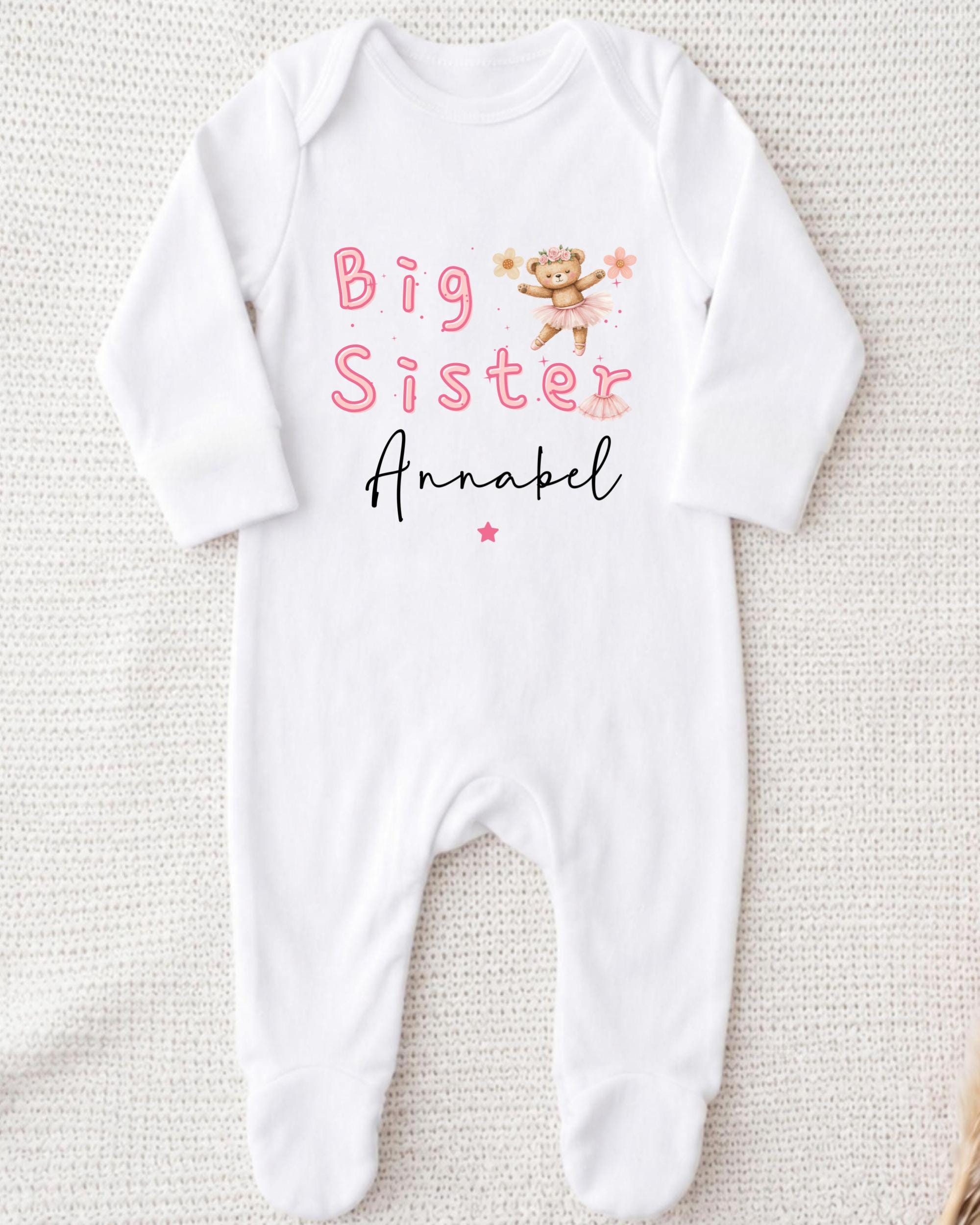 A white onesie with the text "Big Sister Annabel" printed on it, along with a small illustration of a teddy bear.