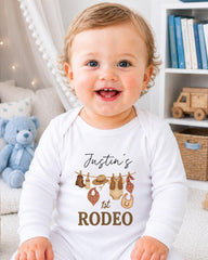 A smiling baby boy wearing a white onesie with a personalized text and graphic design.