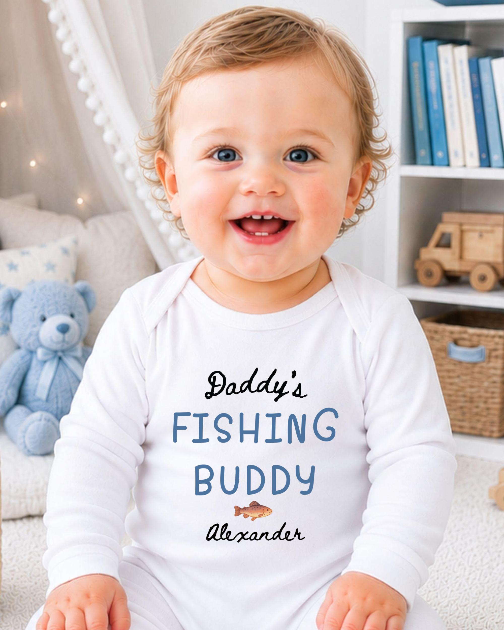 A smiling baby boy wearing a white onesie with the text "Daddys Fishing Buddy Alexander" printed on it.