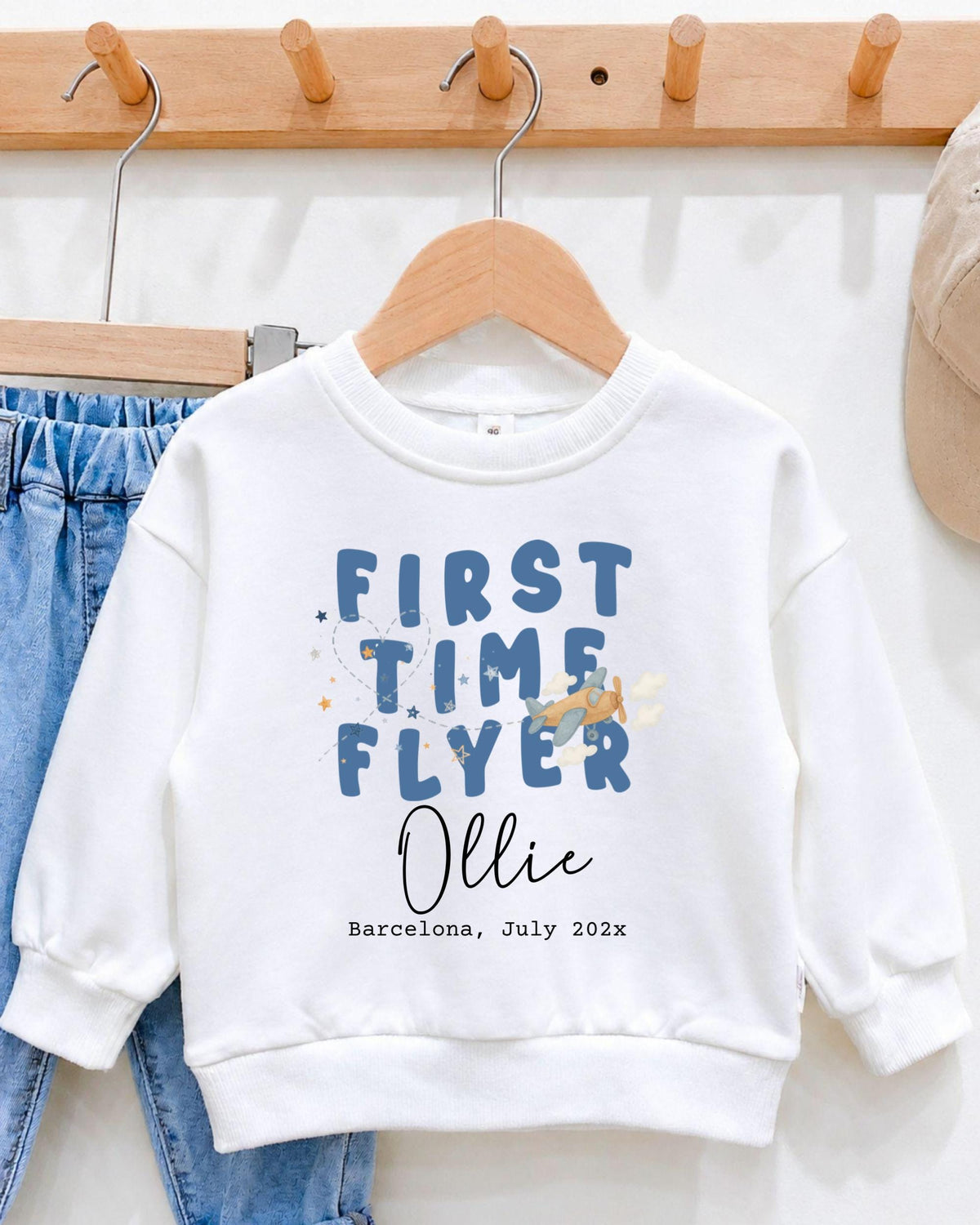 A white sweatshirt with blue text and a graphic design hangs on a wooden hanger.
