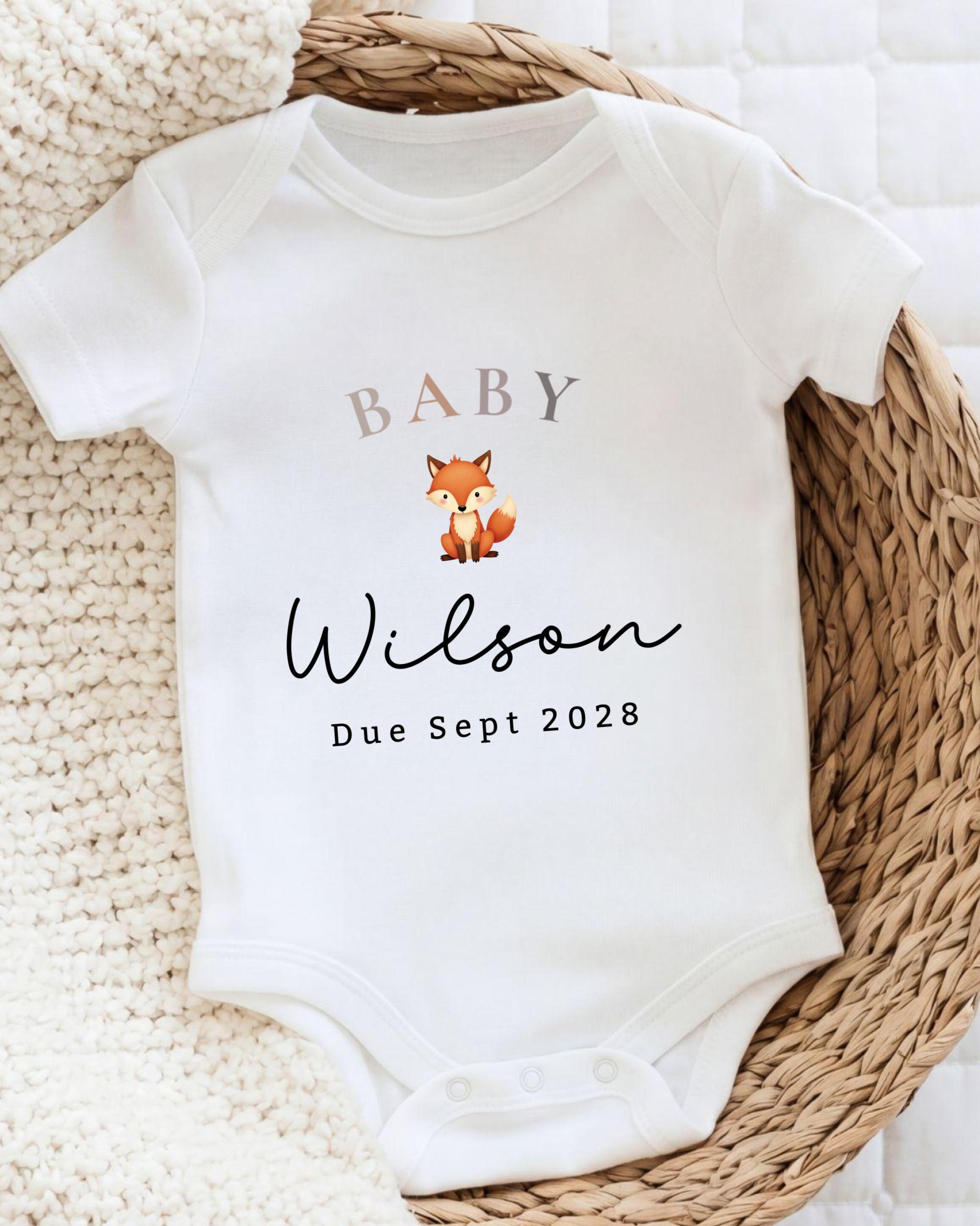 A white baby onesie with the text "BABY Wilson Due Sept 2028" printed on it, along with a small illustration of a fox.