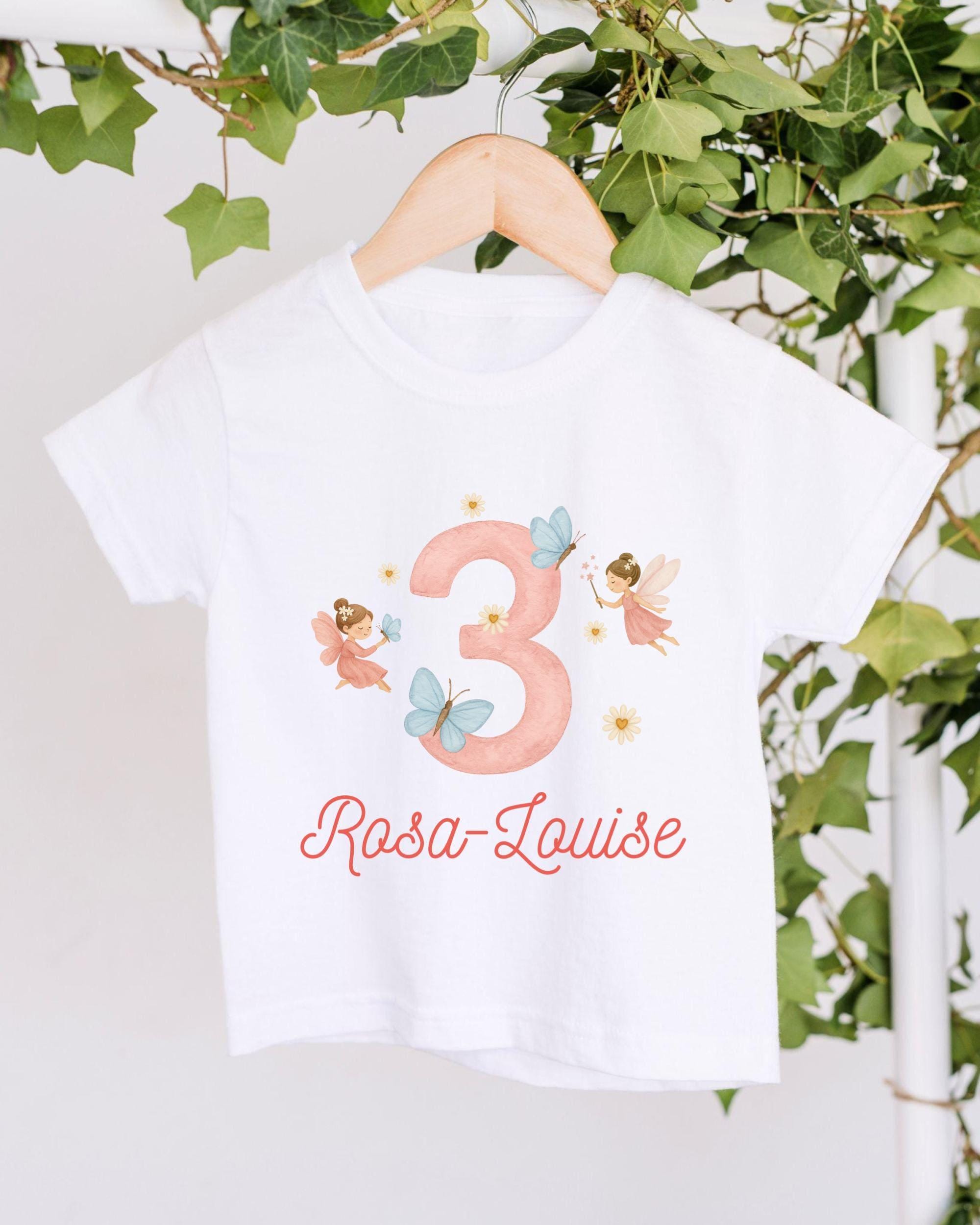 A white t-shirt with a pink number 3 and a design of two angels, along with the text "Rosa Louise" printed on it.