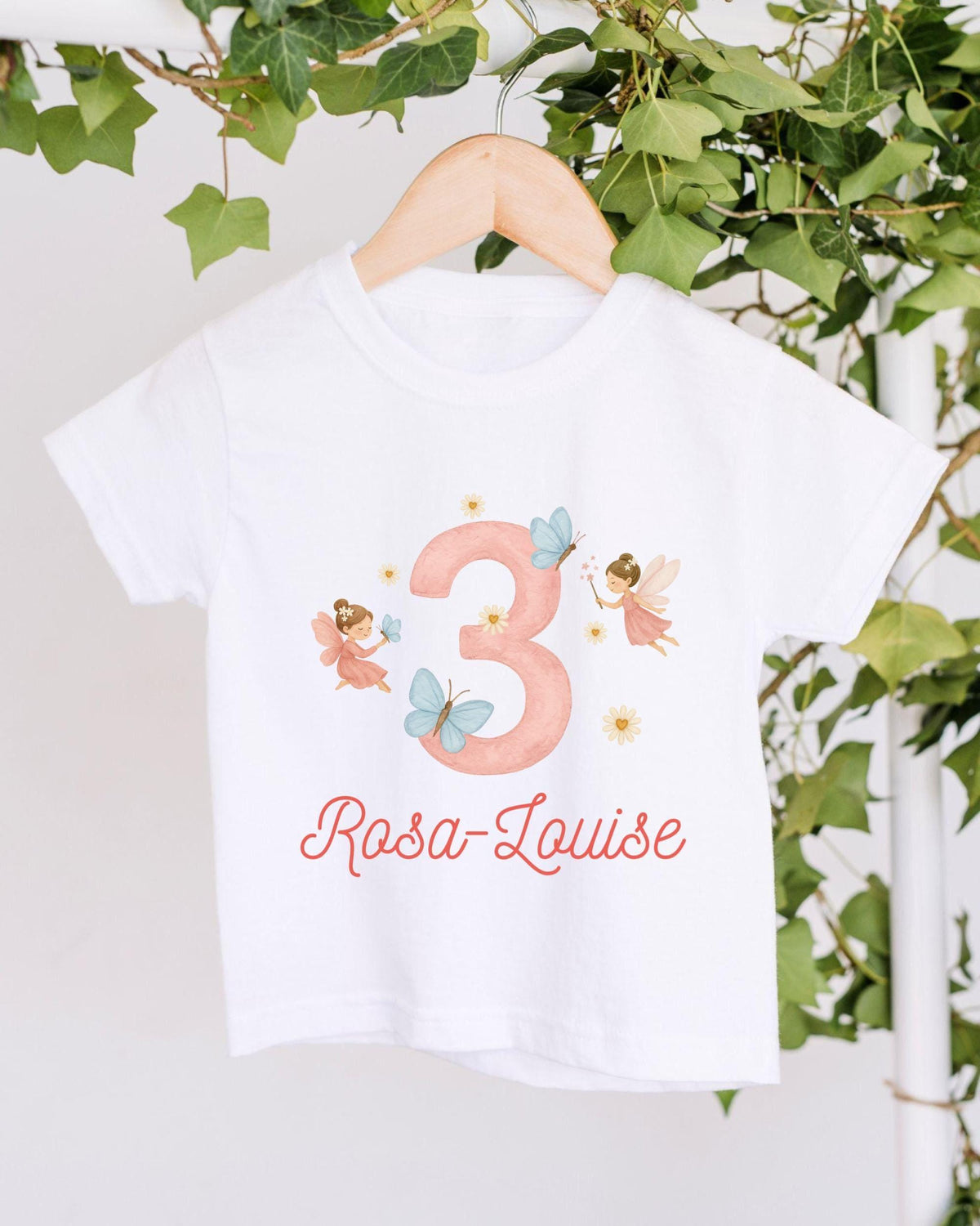 A white t-shirt with a pink number 3 and a design of two angels, along with the text "Rosa Louise" printed on it.