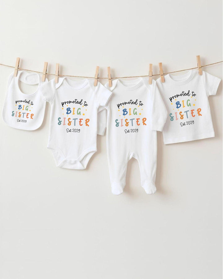 A row of baby clothes with the text "promoted to big sister" printed on them, along with the date "04 2009".