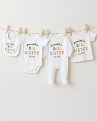 A row of baby clothes with the text "promoted to big sister" printed on them, along with the date "04 2009".